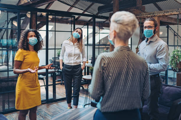Running the business in the state of emergency Group of entrepreneurs wearing masks and standing at a distance in the office fighting photos stock pictures, royalty-free photos & images