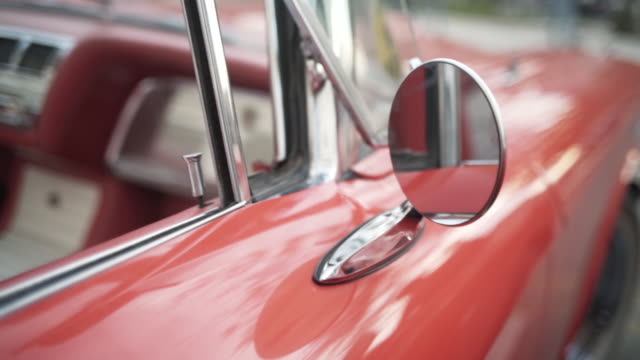 Details of red retro car on a blurred city background. Action. Close up of round rear view mirror of the old fashioned polished shiny red vehicle