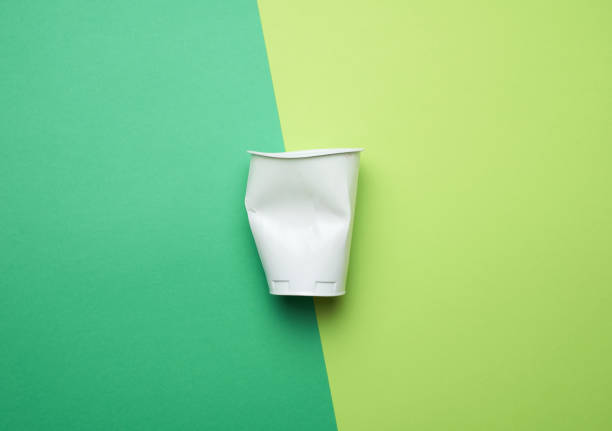 istock crumpled white plastic glass on a green background, flat lay 1255381353