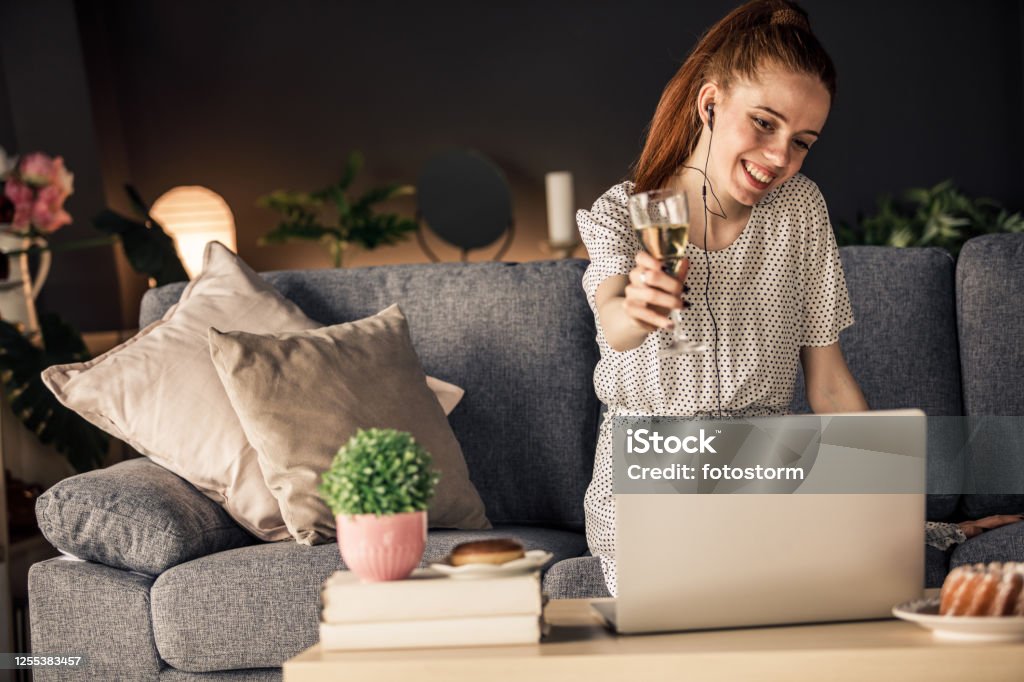 Making a celebratory toast online during lockdown Copy space shot of a cheerful young woman having a celebration event with a friend over a video call. She is making a celebratory toast with a glass of white wine towards laptop camera. Video Call Stock Photo