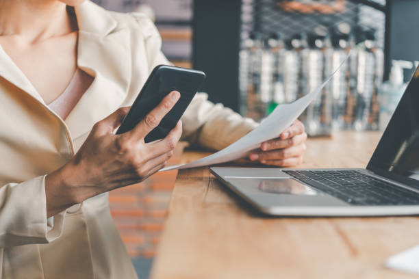 istock Business woman working on smart phone and laptop searching web, browsing information sitting doing work at desk 1255388464