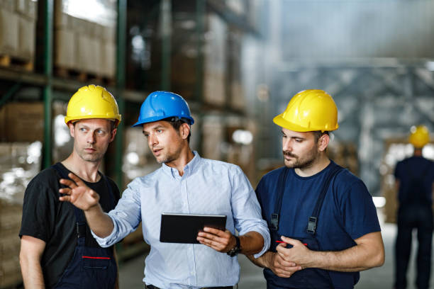istock Male foreman giving instructions to manual workers in distribution warehouse. 1255388713