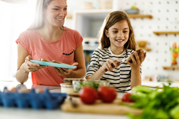 Happy single mother and daughter making breakfast in the kitchen. Happy little girl and her mother preparing sandwiches for breakfast in the kitchen. making a sandwich stock pictures, royalty-free photos & images