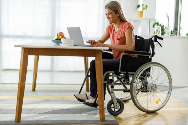 Happy woman in a wheelchair working on laptop at home. Young happy businesswoman in a wheelchair surfing the Internet on a computer while working at home. persons with disabilities photos stock pictures, royalty-free photos & images