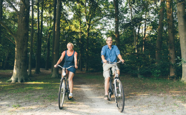 personas mayores activas montando en bicicleta en verano. las personas mayores estilo de vida saludable, deporte y concepto de vida sostenible - action mature adult bicycle senior couple fotografías e imágenes de stock