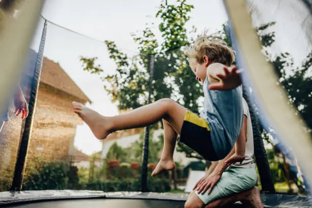 Photo of little boy and his father having fun on the trampoline