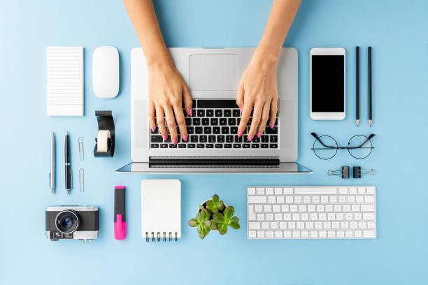 istock Woman’s hands working on laptop on blue table with accessories. Modern workspace. Flat lay 1255401533