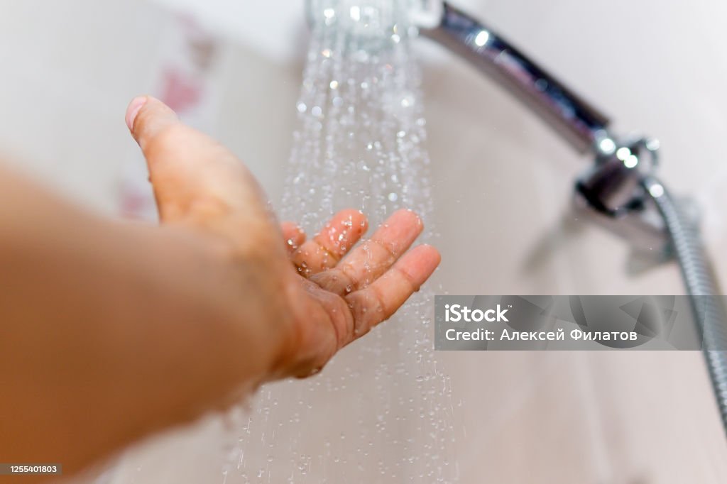 hands check the temperature of the shower water. a man's hand under a stream of water selective focus male and under the stream of water from the shower, checks the water temperature selective focus Shower Stock Photo