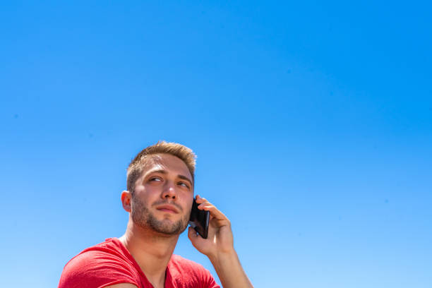 Young male adult with sunglasses using smartphone. The scene is situated on blue background