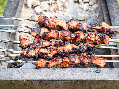 pile of cooked skewered shish kebabs (shashlyk) from pork on outdoor brazier (focus on kebabs on foreground)