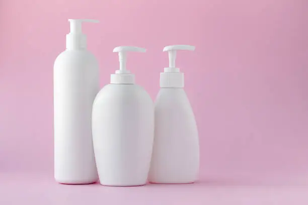 White plastic bottles on a pink background, a set of cosmetic containers with a dispenser. Copy space, empty place for text. Toiletries, pump lotion. Moisturizing cream for body and face