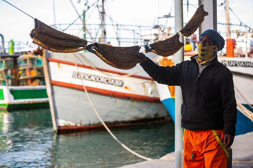 Cape Town, South Africa – July 4: Fisherman selling local delicacy, bokkoms (dried fish) in Kalk Bay Harbour