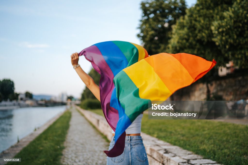 Running with pride Young  lesbian woman with rainbow flag running on city quay LGBTQIA Pride Event Stock Photo