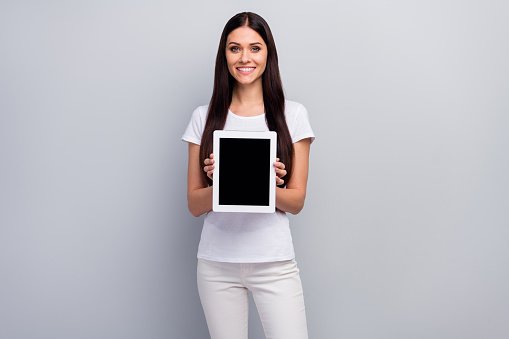 Portrait of her she nice attractive, cheerful cheery lovely pretty straight-haired girl holding in hands demonstrating gadget isolated over light gray pastel color background