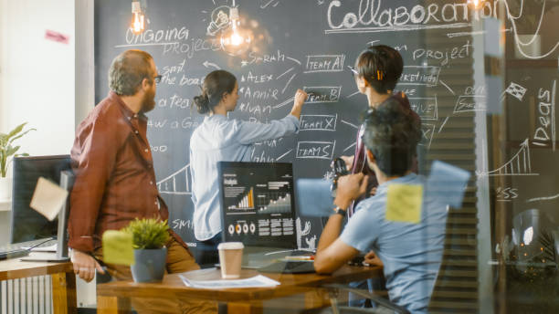 istock Diverse Team of Young Developers Draw Work Plan on a Blackboard Wall, Have Heated Discussion. Creative Office Space with Stylishly Dressed People. 1255413553
