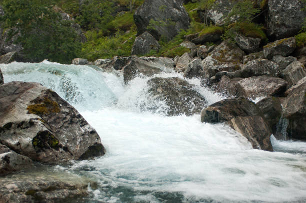 Mountainous rapid river in Norway among the boulders on the background of a green mountain slope