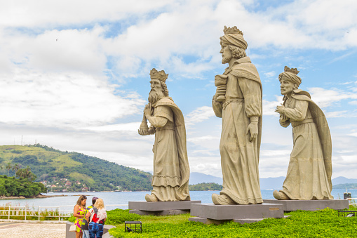 March 5, 2020 - Angra dos Reis, Rio de Janeiro, Brazil: National and international tourists enjoying their vacations and taking a break to take some pictures with Three wise men sculptures in Angra dos Reis, Rio de Janeiro, Brazil. On back, Ilha Grande landscape in a hot summer blue day.