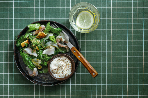 Nordic Salad with Northern Fish, Baked Potatoes, Pickled Cucumber and Smoked Sour Cream. Flat lay top-down composition on dark green tablecloth.