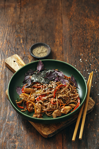 Japanese Yakisoba noodles with chicken and vegetables. Close-up composition on dark wooden background. Vertical image with copy space.