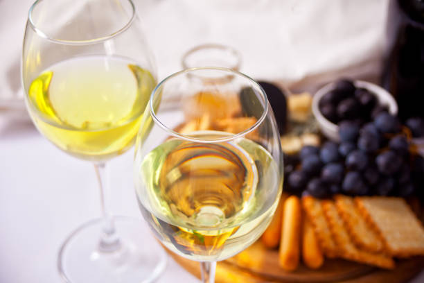 Two glasses of white wine and plate with assorted cheese, fruit and other snacks for party.