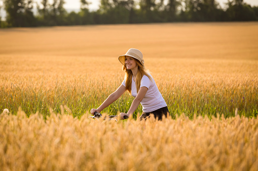 Young girl riding on bike at golden wheat field, summer vacation concept