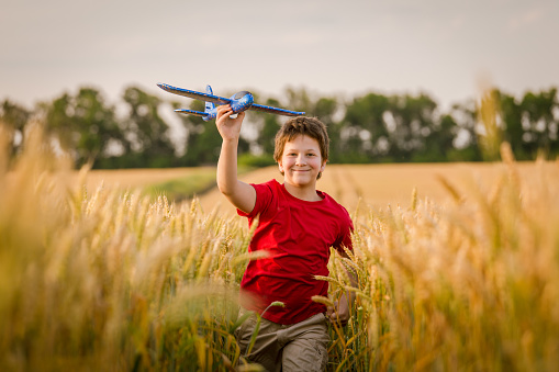 Boy running with toy plane on golden wheat field, summer vacation concept