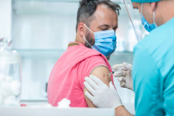 istock Patient with protective face mask looking at his arm while doctor is injecting vaccine 1255423611
