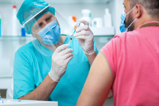 istock Doctor wearing protective workwear pulling COVID-19 vaccine from vial 1255423629