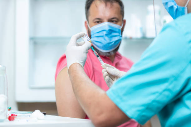 istock Patient with protective face mask looking at doctor pulling COVID-19 from vial with syringe 1255423631