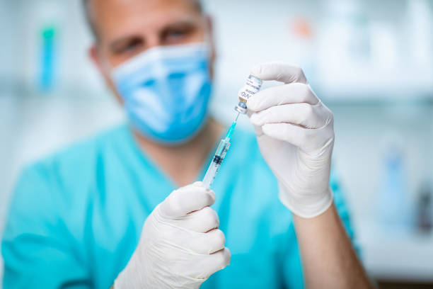 istock Doctor in protective mask and gloves pulling COVID-19 vaccine with syringe 1255423639