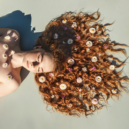 Close up portrait of young ginger curly girl with flowers in hair above. Top view. Concept of spring and summer youth happiness.