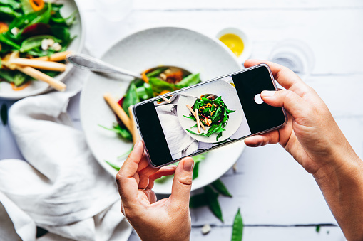 Woman taking photograph of a healthy green salad with her cell phone. Close-up of female hands photographing a plate of salad with mobile phone.