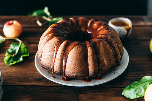 Close-up of a apple bundt cake with caramel sauce in the kitchen. Tasty apple cake on a wooden table.