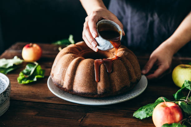Shot of a woman pouring caramel sauce over apple bundt cake in the kitchen. Female hands preparing delicious apple cake.