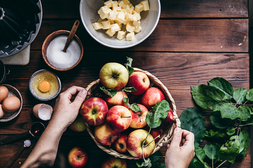 Directly above shot of woman with a basket full of freshly picked apples on table with cake baking ingredients. Woman baking cake with freshly picked apples.