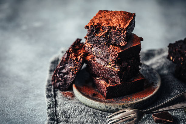 Delicious chocolate zucchini brownies Pile of freshly made chocolate zucchini brownies garnished with cocoa powder on a round wooden plate. Delicious chocolate zucchini brownies served. vegan food photos stock pictures, royalty-free photos & images