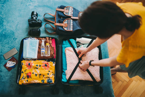 Woman packing suitcase for travel Woman packing suitcase for summer travel, including face masks and airplane travel-sized antibacterial hand gels packing stock pictures, royalty-free photos & images