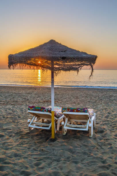 Sunset on the beach in Torremolinos, Spain sunbed and umbrella on the sunset background, Torremolinos, Spain torremolinos beach stock pictures, royalty-free photos & images