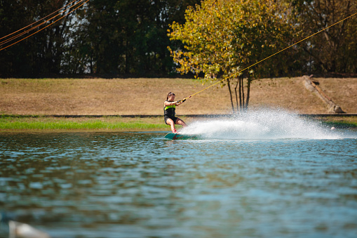 Young woman pulled by towing cable tilted backwards on wakeboard making a splash on the lake surface