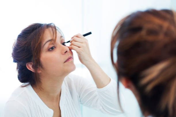 istock Beautiful young woman applying make up before leaving her home 1255442444