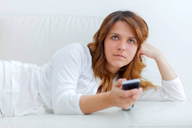 istock Young woman lying on couch watching TV looking bored 1255442462