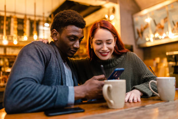 istock Charming multiracial heterosexual couple looking at funny content at mobile phone while spending their free time at the coffee shop 1255449985
