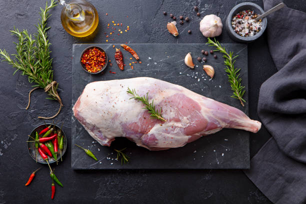 istock Raw lamb leg with spices and herbs on marble cutting board. Dark background. Top view. 1255452045