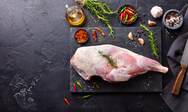istock Raw lamb leg with spices and herbs on marble cutting board. Dark background. Copy space. Top view. 1255452297