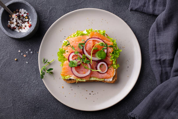 Sandwich with salmon, vegetables and cream cheese on plate. Dark background. Top view.