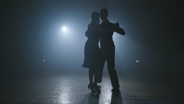 Woman and man doing professional movements while dancing tango in smoky ballroom