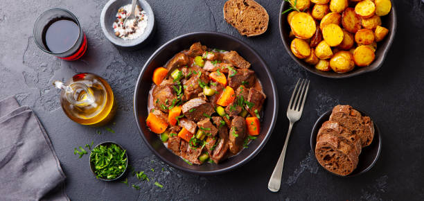 carne bovina e legumes ensopados em tigela preta com batatas de bebê assadas. fundo escuro. vista superior. - prepared potato vegetable meat food - fotografias e filmes do acervo