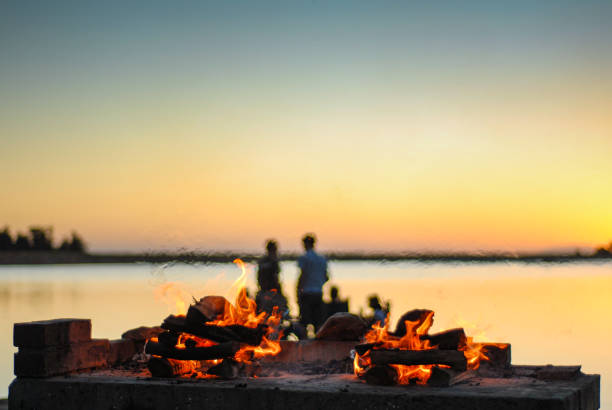 Braai Barbecue fire on a fireplace next to a lake at sunset with silhouette people mirage behind Braai Barbecue fire on a fireplace next to a lake at sunset with silhouette people on a jetty mirage behind south african braai stock pictures, royalty-free photos & images