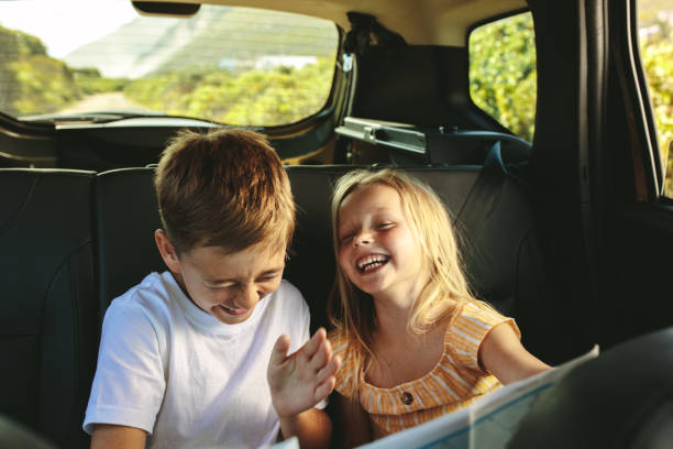 Kids enjoying while travelling by car Small boy and girl sitting on backseat of car looking at map and smiling. Kids traveling in a car on roadtrip playing with a map. kids laughing stock pictures, royalty-free photos & images