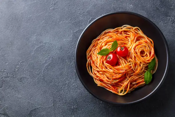 Photo of Pasta, spaghetti with tomato sauce in black bowl. Grey background. Copy space. Top view.